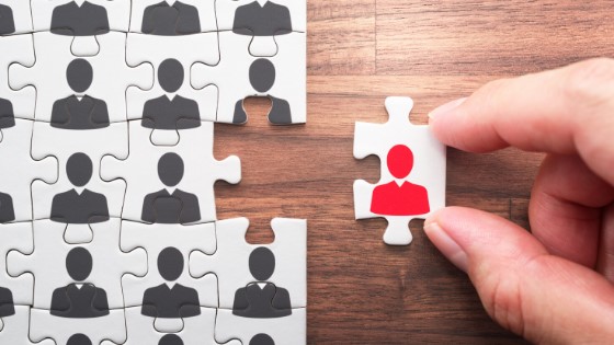 A person adds a red figure to a puzzle piece, illustrating the importance of fitting the right talent into a team
